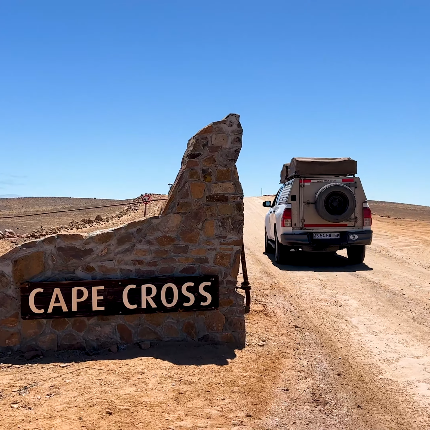 4x4 Toyota Hilux vehicle driving past the Cape Cross entrance sign on a sandy road in Namibia.